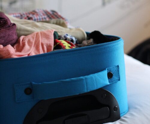 blauwe koffer met kleding er in op bed